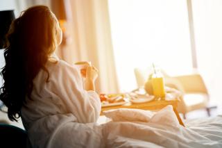 woman watching sunrise from hotel bed with breakfast