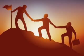 three business people helping each other climb a mountain